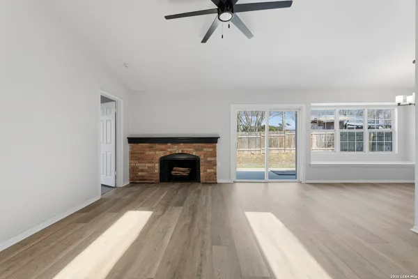 a view of an empty room with wooden floor fireplace and a window