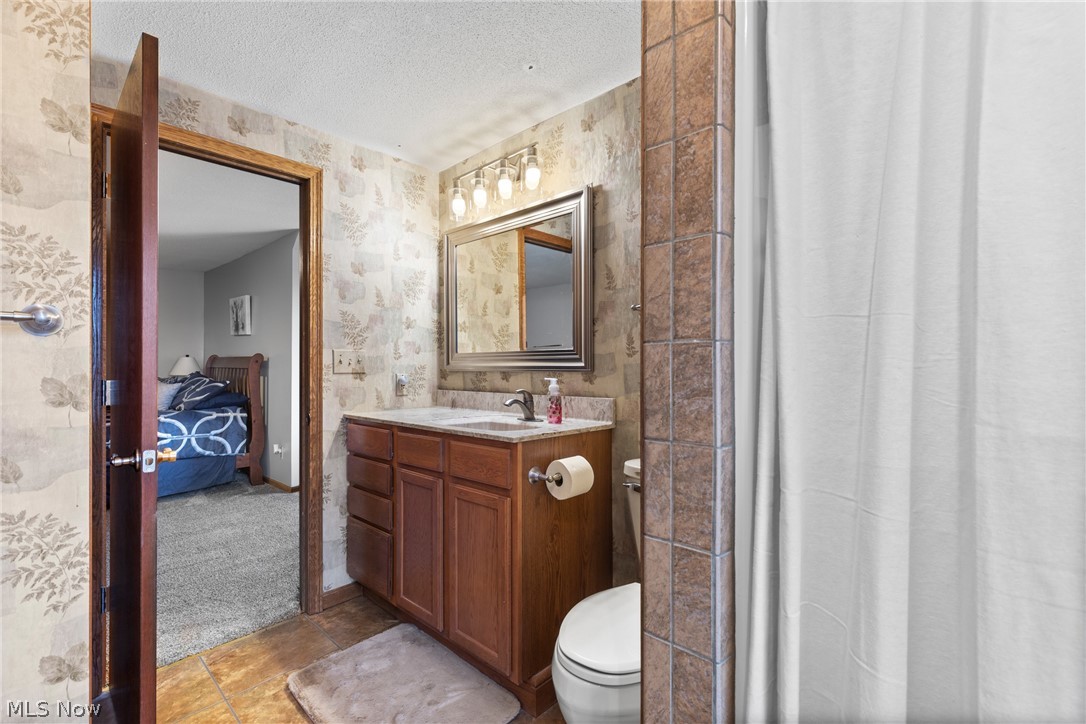64508 Slade Road Cambridge, OH 43725 - Photo 26 of 50 Ensuite bathroom with vanity, a textured ceiling, a shower with curtain, wallpapered walls, and light colored carpet