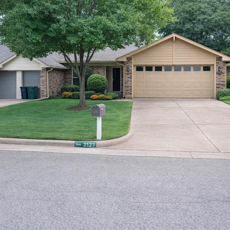 Brick and siding exterior featuring a two-car garage with panel windows, a concrete driveway, a manicured lawn, and mature landscaping