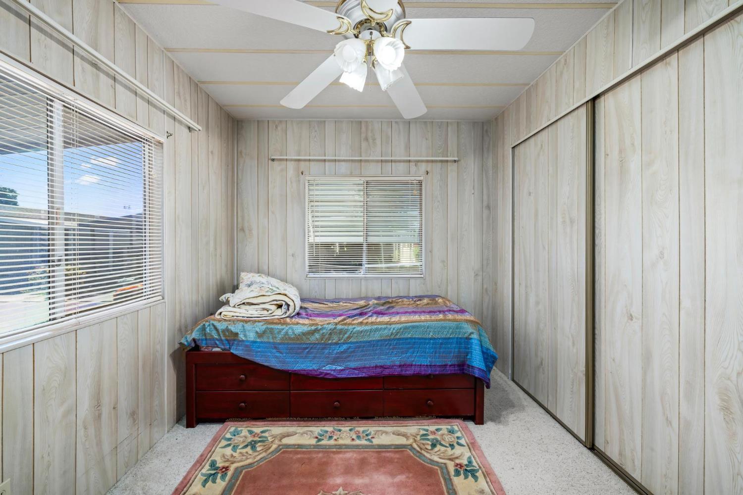1200 South Carpenter Road, Unit 4 Modesto, CA 95351 - Photo 20 of 31 Bedroom featuring light wood-paneling walls and ceiling, a ceiling fan with integrated lighting, two windows with horizontal blinds, and a built-in closet with sliding doors