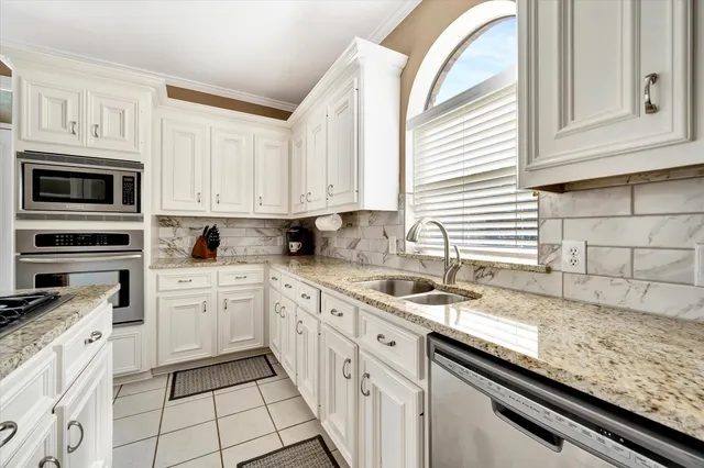 a kitchen with granite countertop white cabinets stainless steel appliances a sink and a window