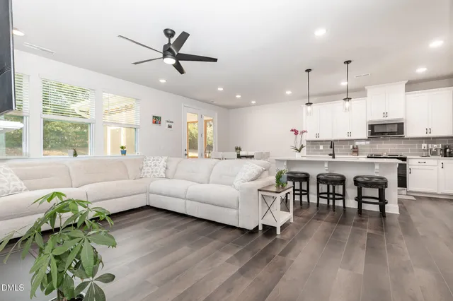 a living room with couches kitchen view and a large window