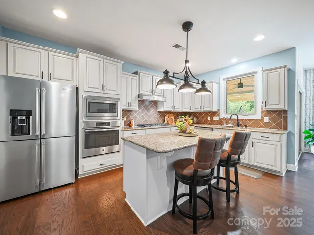 a kitchen with stainless steel appliances granite countertop a refrigerator a sink dishwasher a stove and white cabinets with wooden floor