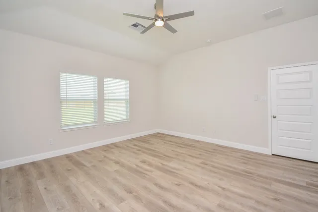 an empty room with wooden floor ceiling fan and windows