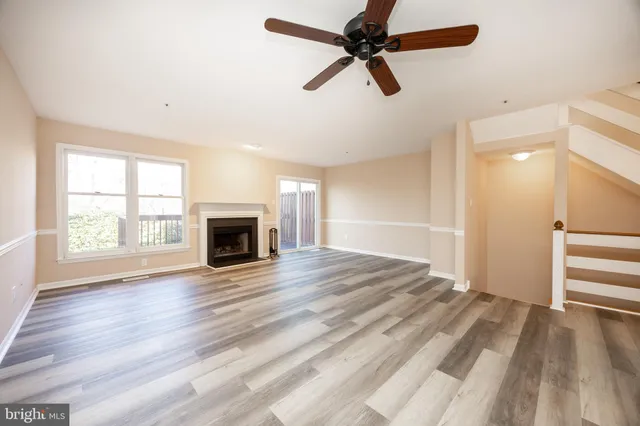 an empty room with wooden floor fan and windows