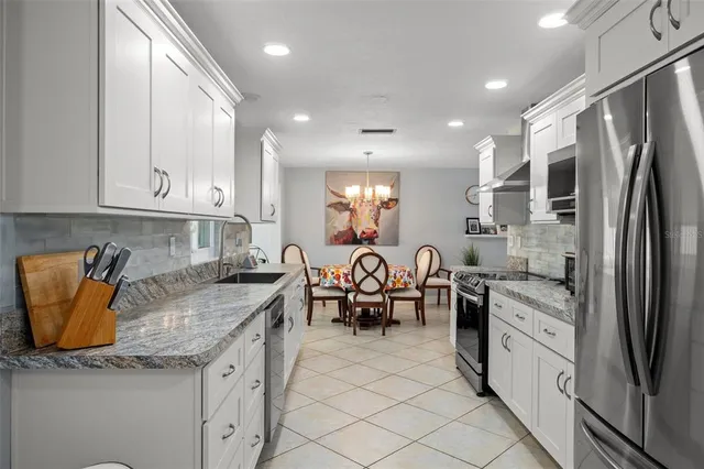 a kitchen with granite countertop a refrigerator a stove a sink a dining table and chairs