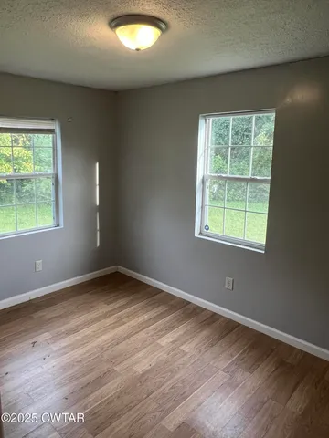 an empty room with wooden floor fan and windows