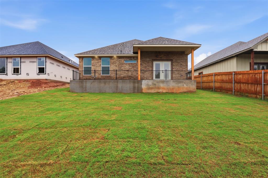 1413 Ridgeview Circle Granbury, TX 76048 - Photo 26 of 35 Expansive backyard featuring a manicured lawn, a raised patio with black metal railing, and a covered porch with wood columns