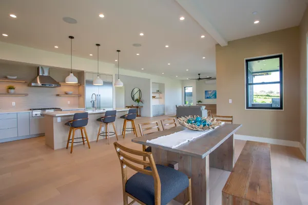 a kitchen with stainless steel appliances kitchen island granite countertop a stove a refrigerator a sink a dining table and chairs with wooden floor