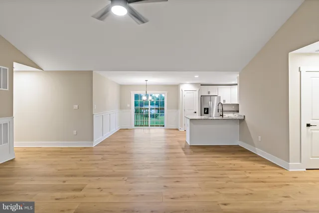 a view of kitchen and empty room with wooden floor and fan