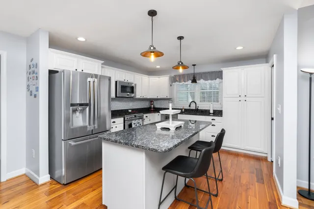 a kitchen with stainless steel appliances granite countertop a refrigerator a sink dishwasher a stove and a dining table with wooden floor