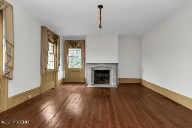 a view of an empty room with wooden floor fireplace and a window