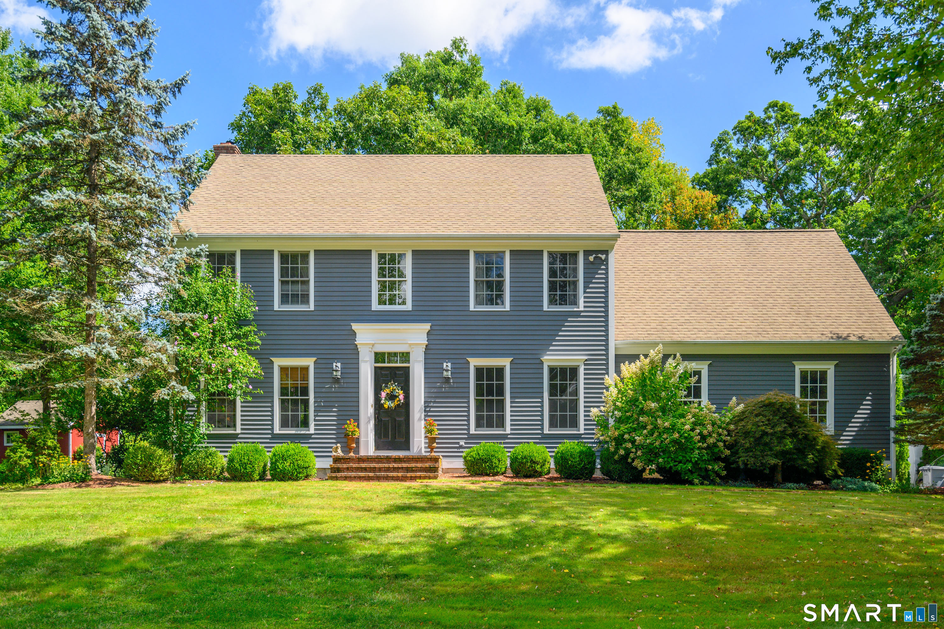 Expansive front lawn with mature trees and classic Colonial facade set back from the road.