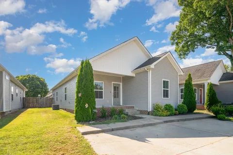 a view of yellow house with a yard plants and large tree
