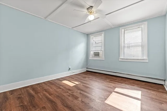 an empty room with wooden floor ceiling fan and windows