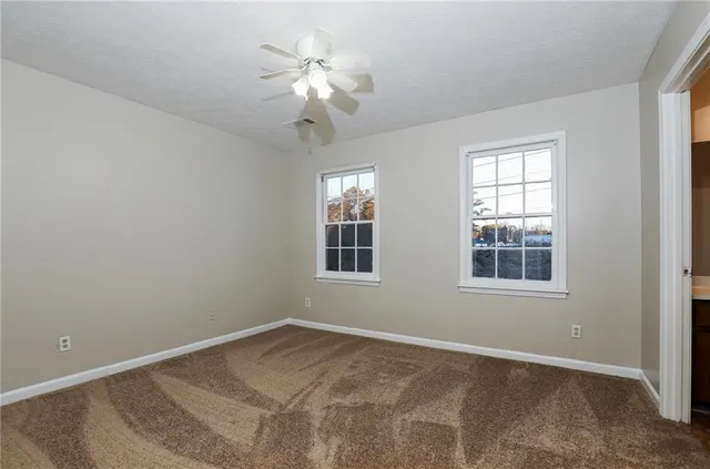 an empty room with chandelier fan and windows