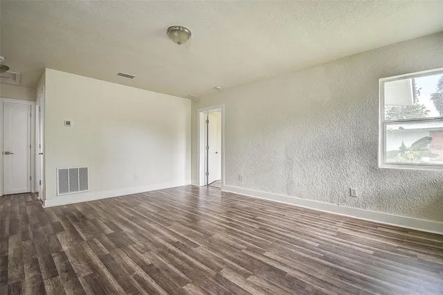 a view of an empty room with wooden floor and a window