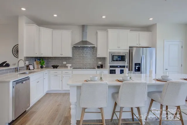 a kitchen with stainless steel appliances a sink a stove a refrigerator cabinets and a dining table with wooden floor
