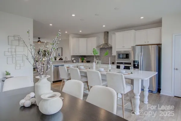 a large white kitchen with stainless steel appliances kitchen island granite countertop a dining table chairs and a refrigerator