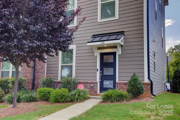 a view of a house with brick walls and a yard with plants and large tree