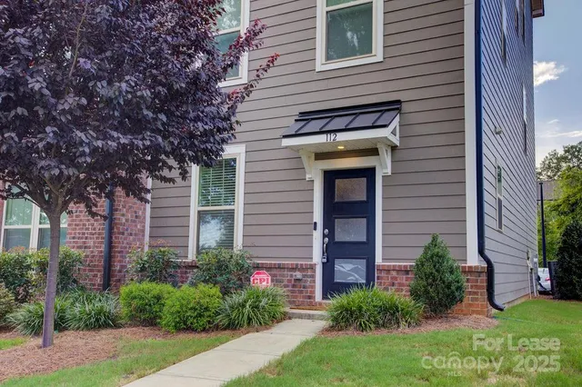 a view of a house with brick walls and a yard with plants and large tree