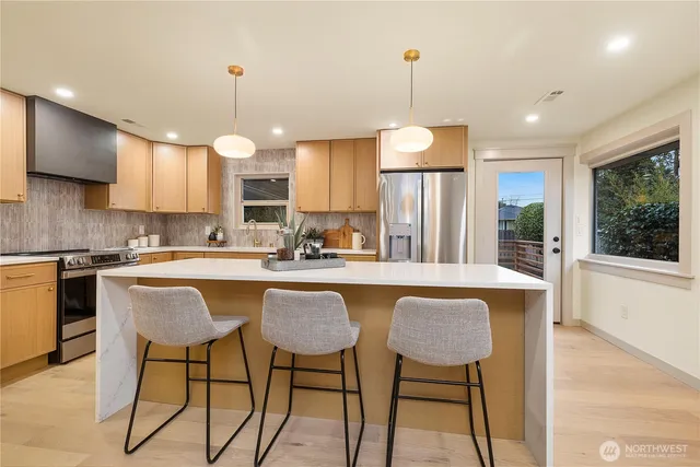 a kitchen with stainless steel appliances granite countertop a stove a sink a refrigerator a kitchen island with a dining table and chairs