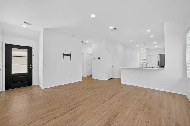 a view of an empty room with wooden floor and kitchen