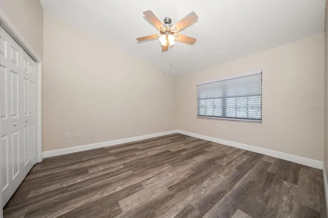 an empty room with wooden floor chandelier fan and windows
