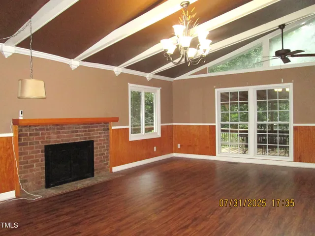 a view of an empty room with wooden floor fireplace and a window