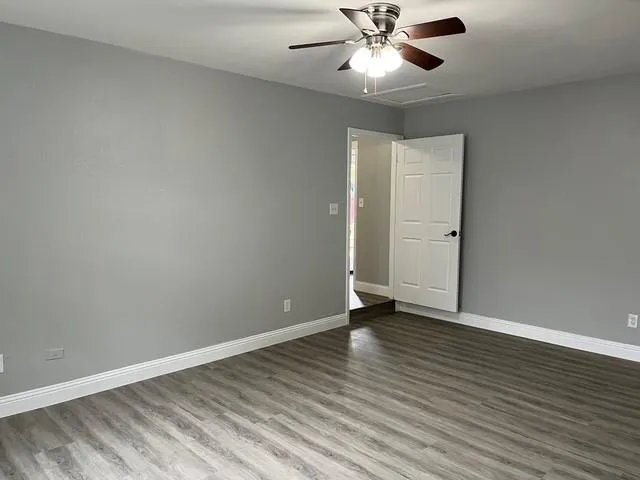 an empty room with wooden floor chandelier fan and windows