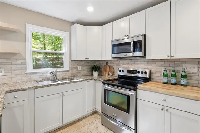 a kitchen with stainless steel appliances granite countertop white cabinets a stove a sink and a window