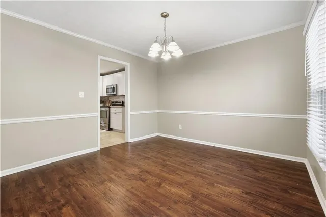 an empty room with wooden floor chandelier and windows