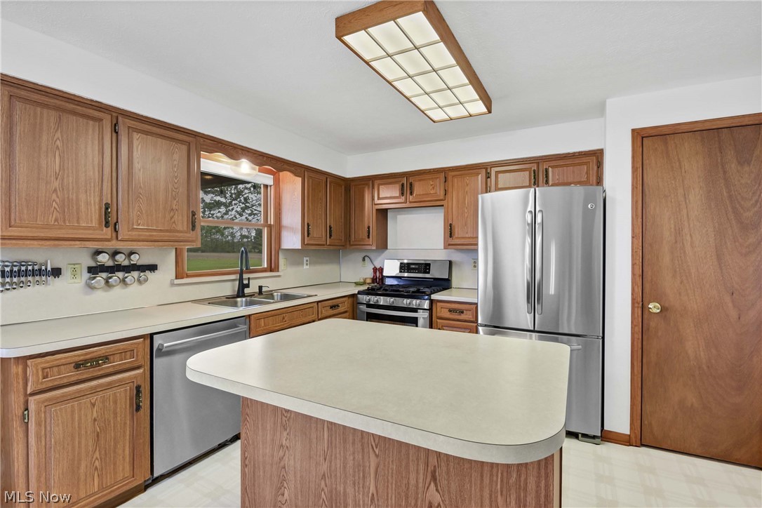 9550 Spencer Road Homerville, OH 44235 - Photo 15 of 50 Kitchen featuring wood-finish cabinetry, a center island with a light-toned countertop, a double basin sink with a gooseneck faucet, and overhead fluorescent lighting
