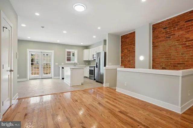 a view of an empty room with wooden floor and a kitchen