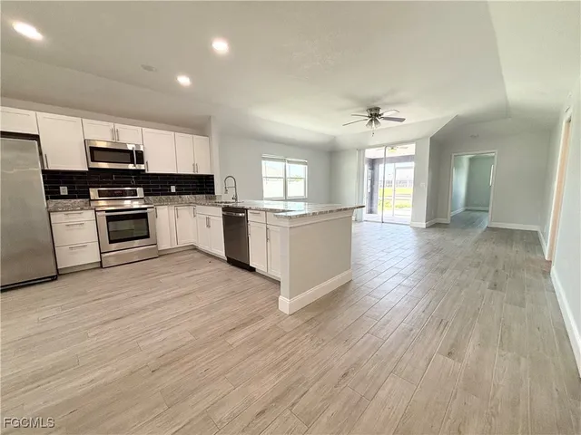 a kitchen with stainless steel appliances granite countertop a stove top oven a sink dishwasher and a refrigerator with wooden floor