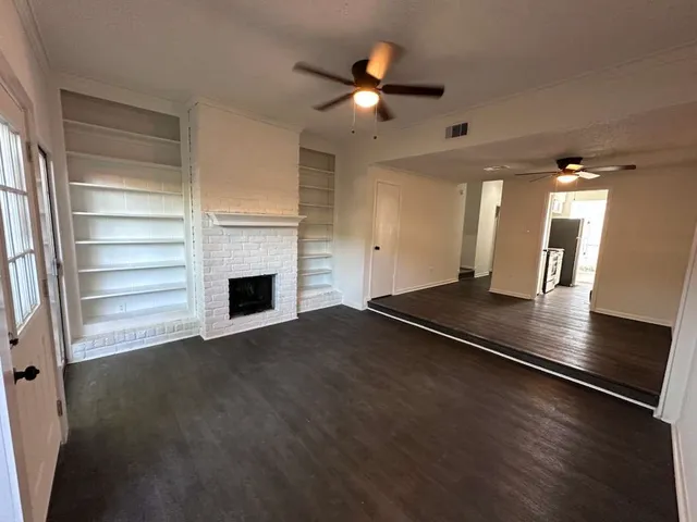 a view of an empty room with a fireplace and a ceiling fan