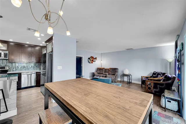 a kitchen with stainless steel appliances kitchen island granite countertop a stove a refrigerator a oven a dining table and chairs with wooden floor