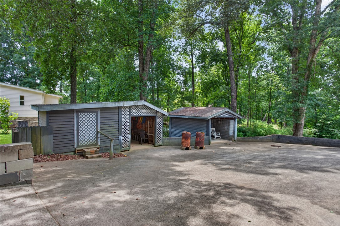 230 Dickard Road Seneca, SC 29672 - Photo 4 of 25 Functional sheds and ample paved space provide practical utility amidst a verdant backdrop.