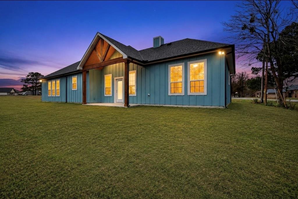 335 Cross Tie Ranch Road Trinidad, TX 75163 - Photo 29 of 30 Rear exterior featuring blue vertical board and batten siding, a covered patio with wood beams, a dark shingle roof, and multiple windows