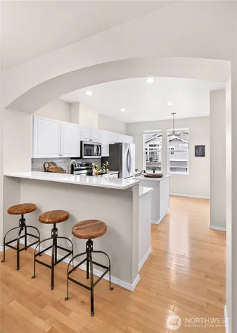 a kitchen with stainless steel appliances kitchen island granite countertop a refrigerator a stove a sink and white cabinets with wooden floor