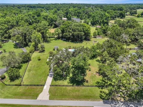 an aerial view of a residential houses with outdoor space and trees all around