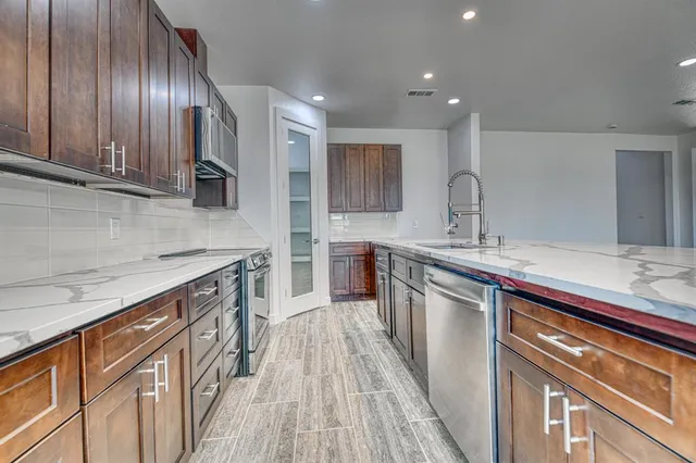 a kitchen with kitchen island granite countertop a sink stainless steel appliances wooden floor and cabinets