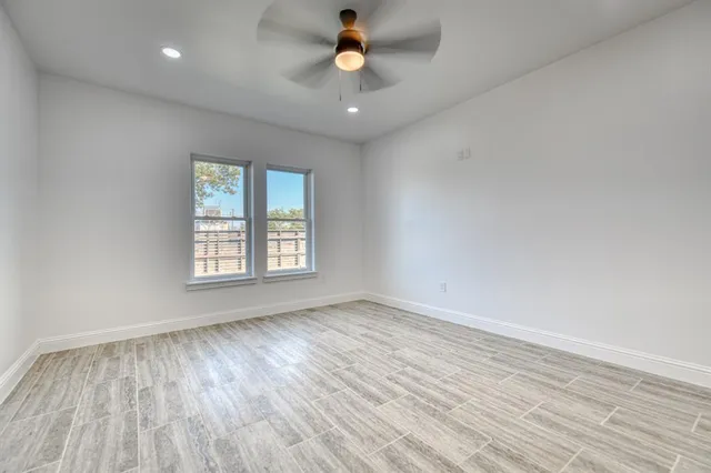 an empty room with wooden floor ceiling fan and windows