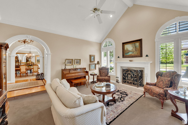 7740 Keswick Road Sandy, UT 84093 - Photo 14 of 74 Vaulted ceilings featuring a ceiling fan, arched windows with plantation shutters, a fireplace with an ornate screen and mantel, and an arched entry to a formal dining room with wood-finish flooring