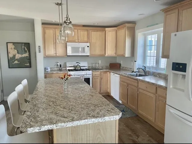 a large kitchen with kitchen island granite countertop a sink a counter top space appliances and cabinets