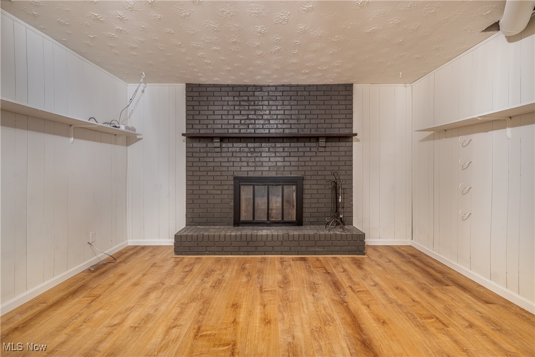 24534 Mill Road Utica, OH 43080 - Photo 23 of 38 Unfurnished living room featuring a textured ceiling, light wood-style floors, wooden walls, and a fireplace