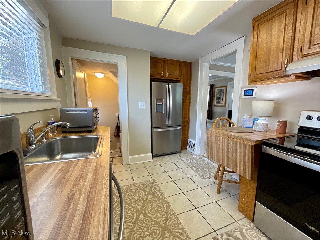 904 Chalker Street Akron, OH 44310 - Photo 19 of 28 Kitchen with appliances with stainless steel finishes, brown cabinetry, light tile patterned floors, wood counters, and under cabinet range hood