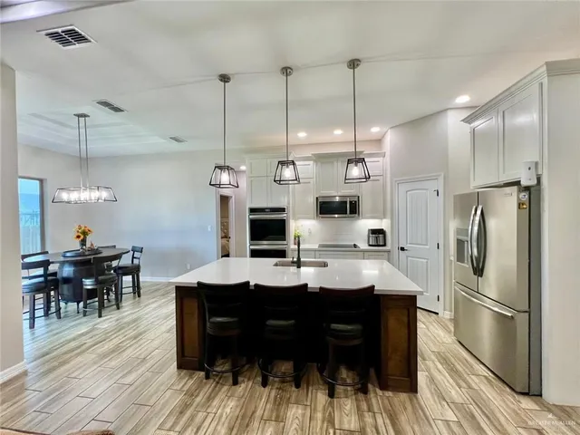 a kitchen with stainless steel appliances kitchen island granite countertop a refrigerator a stove and a dining table with wooden floor