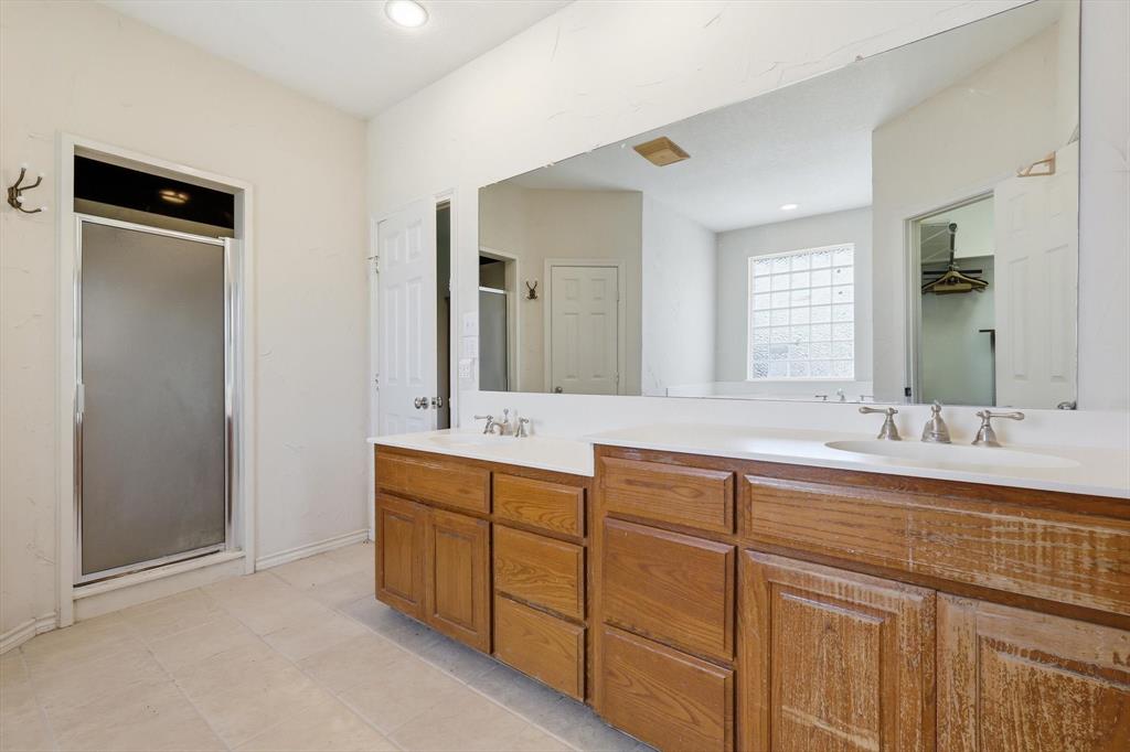 12190 Bell Road Pilot Point, TX 76258 - Photo 26 of 39 Bathroom featuring dual wood-finish vanities with integrated sinks, a large mirror, a shower with a frosted glass door, and a glass block window