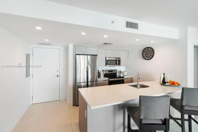 a kitchen with stainless steel appliances kitchen island granite countertop a dining table chairs and a refrigerator